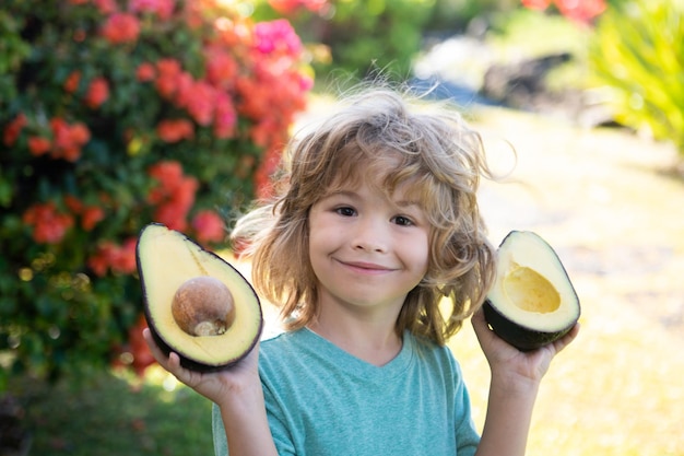 Happy child boy on the yard having fun with avocado. Kids summer vitamin.