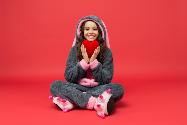 Happy child in bunny pajamas hold red heart lifesaving gift donation