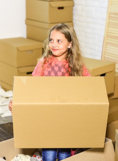 Счастливый ребенок картонная коробка играет в новый дом новая квартира счастливая маленькая девочка Картонные коробки переезжают в новый дом покупка нового жилья девочка держит огромную коробку