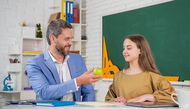 Photo happy child in classroom with tutor sharing apple