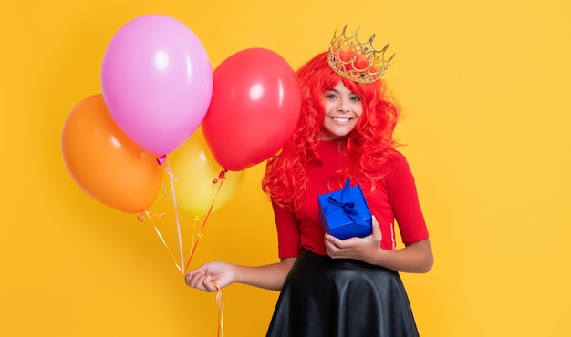 Happy child in crown with gift box and party balloon on yellow background