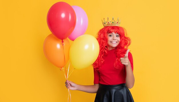 Happy child in crown with party balloon on yellow background