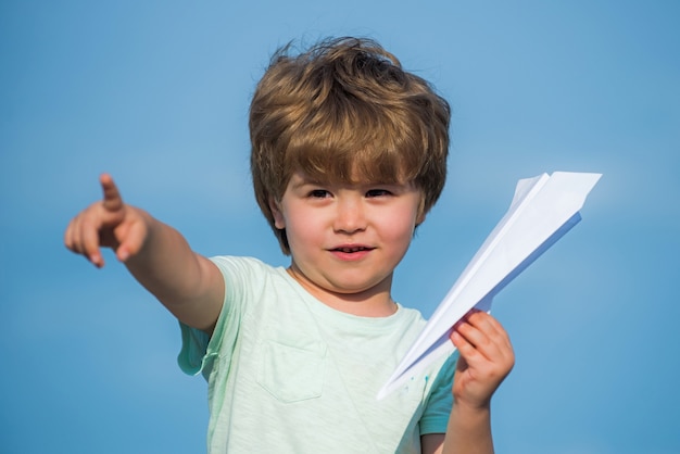 Happy child. cute boy with paper aipplene. happy child with\
paper toy airplane looking at camera. childhood concept. dreams of\
traveling. happy kid on summer field - dream of flying\
concept.