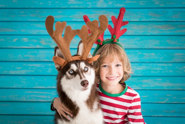 クリスマスイブの子供と犬の幸せな子供とサンタクロースの帽子の赤ちゃんに身を包んだペットがhを楽しんでいます