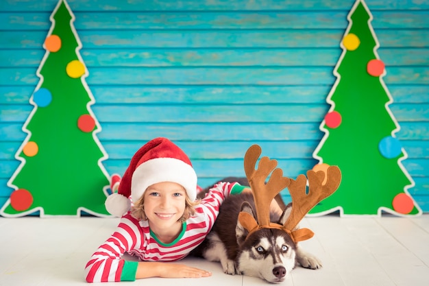 サンタクロースの帽子に身を包んだクリスマスイブの子供とペットの幸せな子供と犬