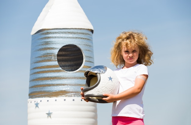 Happy child dressed in an astronaut costume playing with hand made rocket