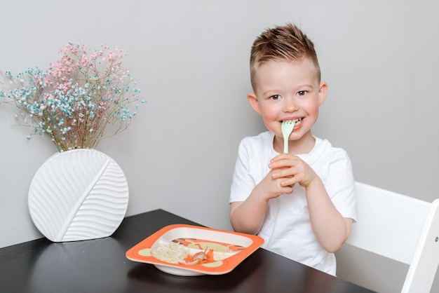 Happy child eating delicious pasta at the table in the kitchen