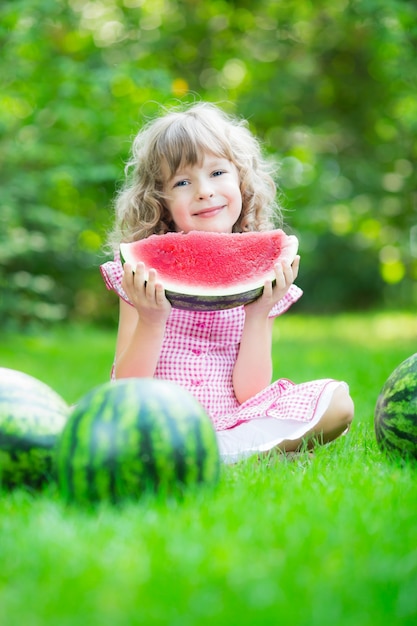 Happy child eating watermelon outdoors in summer park