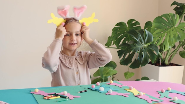 Photo happy child girl in bunny ears make and play easter paper colored garland easter bunny