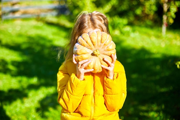 Happy child girl covers the face with pumpkin outdoors in halloween