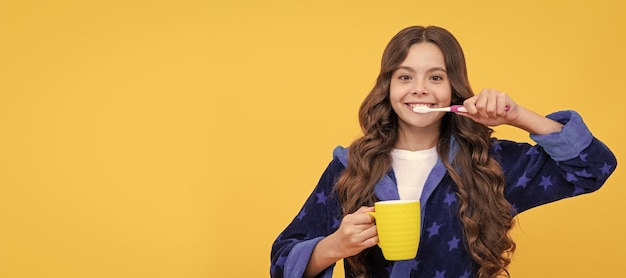 Happy child girl in cozy bathrobe use toothbrush and cup personal care Banner of child girl with teeth brush studio portrait header with copy space