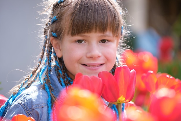 Happy child girl enjoying sweet smell of red tulip flowers in summer garden