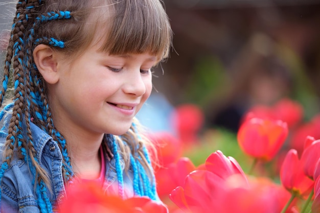 Bambina felice che gode del dolce profumo dei fiori di tulipano rosso nel giardino estivo