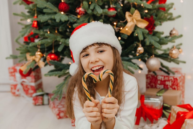 幸せな子の女の子は、クリスマスのキャンディケインを保持しています。クリスマスの前夜に幸せな幸せな少女。希望に満ちた子供。大晦日。