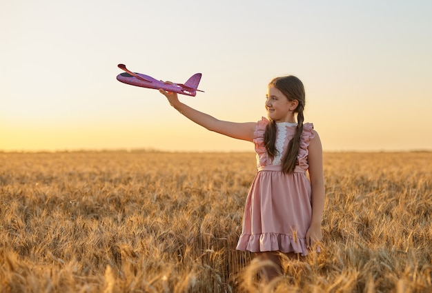 Happy child, girl playing with toy airplane on summer wheat field. Little Daughter dreams of flying. Carefree kid playing outdoors