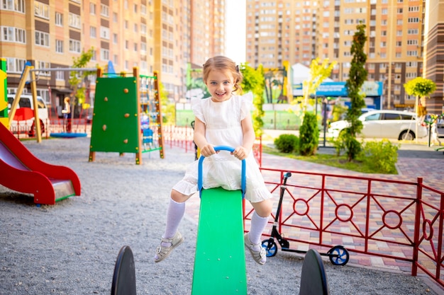 A happy child girl plays at the children's complex playground near the house in the summer in the yard and smiles