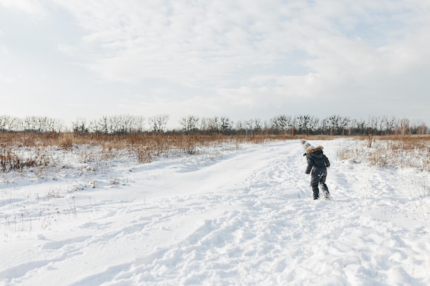 雪の降る冬の散歩で幸せな子供の女の子 クールな黒い雪のオーバーオールを着て 冬の服装