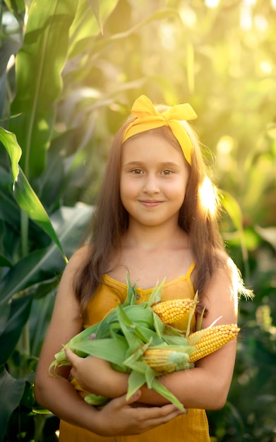 happy child girl stands in the thickets of corn and holds a yellow cob of corn in her hands