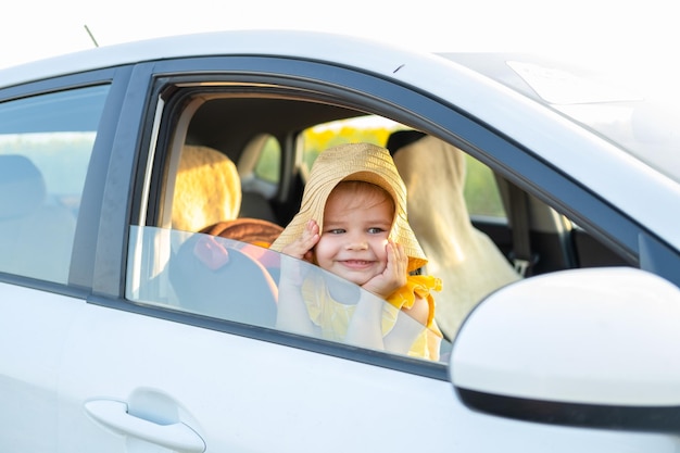 Photo happy child girl in straw hat looking out of a car window in summer nature at sunset