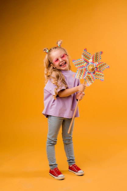 happy child girl in sunglasses holding a baby windmill on a yellow space