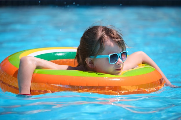 Happy child girl swimming on inflatable circle in swimming pool on sunny summer day during tropical vacations