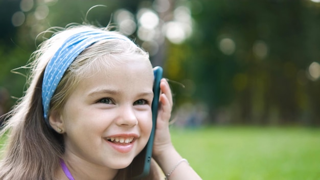 Счастливая девочка ребенка разговаривает по мобильному телефону в летнем парке.