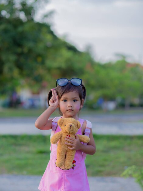 Happy child girl with hugging teddy bear in dress in summer garden outdoor