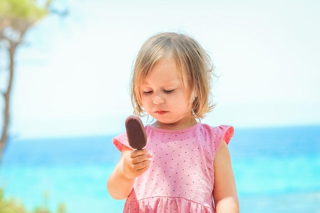 公園の旅で自然の海のそばでアイスクリームを持つ幸せな子供の女の子