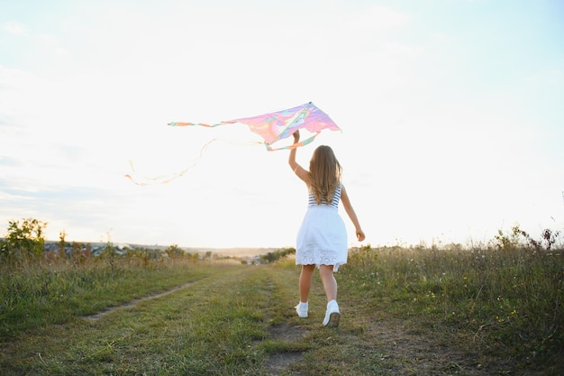 Happy child girl with a kite running on meadow in summer in nature