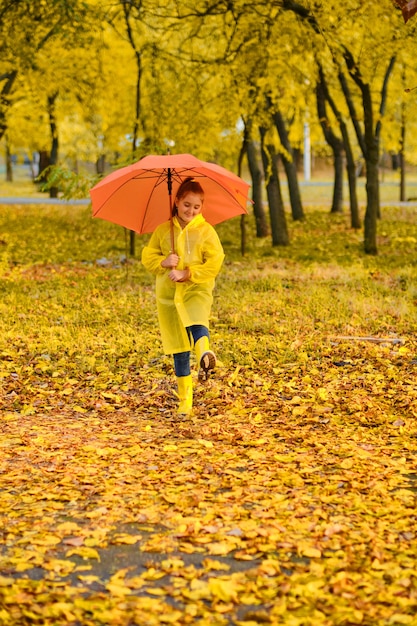 Happy child girl with an umbrella and rubber boots on an autumn walk