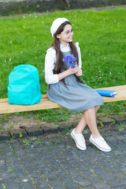 안경을 쓴 행복한 아이는 꽃 교사의 날 공원 벤치에서 휴식을 취합니다
