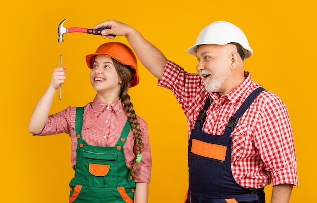 Happy child and grandfather carpenter in helmet on yellow background