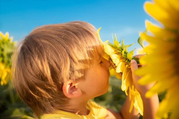 Happy child having fun in spring field of sunflowers. Outdoor portrait of kid against blue sky background