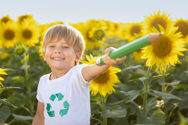 Happy child having fun in spring field of sunflowers. Outdoor portrait of kid against blue sky background