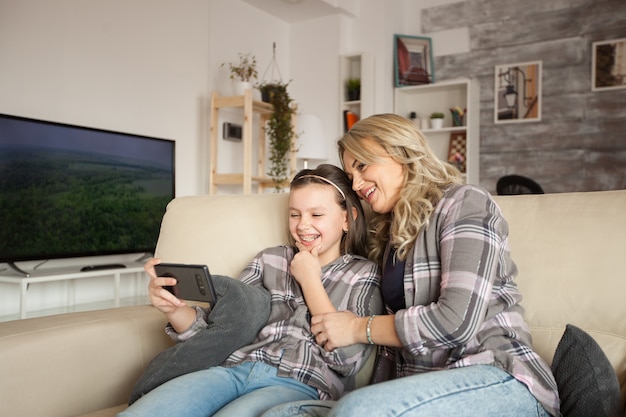 Photo happy child and her mother watching a funny video on smartphone.