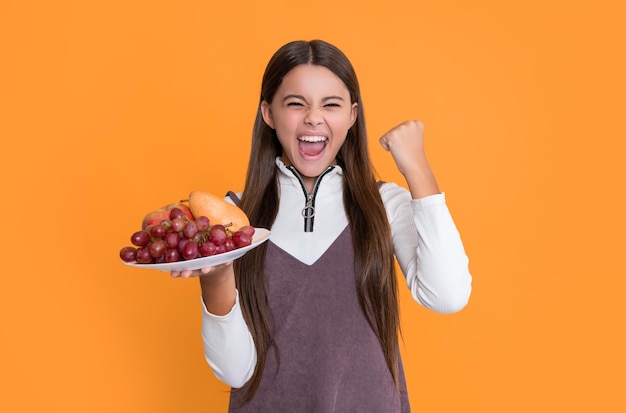 Happy child hold fresh fruit plate on yellow background vitamins