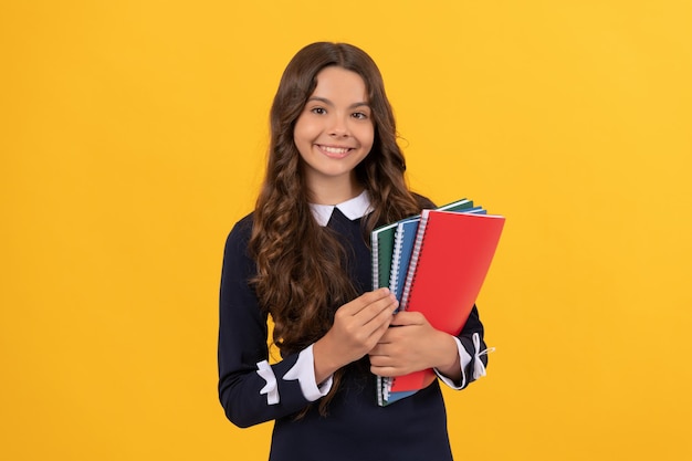 Happy child hold school copybooks for homework studying on yellow background, school