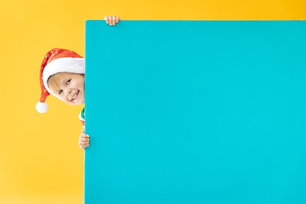 Happy child holding blue banner blank against yellow background. Christmas greeting card concept
