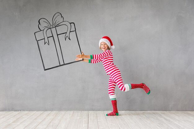 Happy child holding Christmas gift box. Funny kid playing at home
