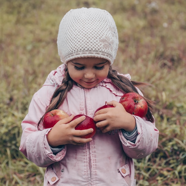 Happy child holding red apples in his hands. Harvest Funny kid outdoors in autumn park.