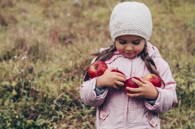 Happy child holding red apples in his hands. harvest funny kid outdoors in autumn park.