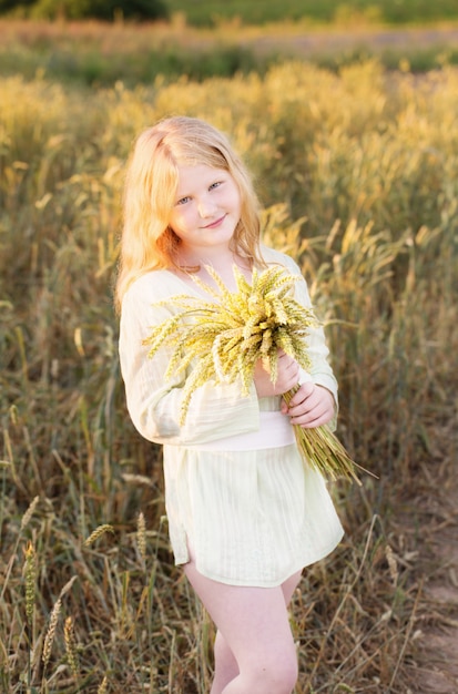 Happy child holding wheat ears at field