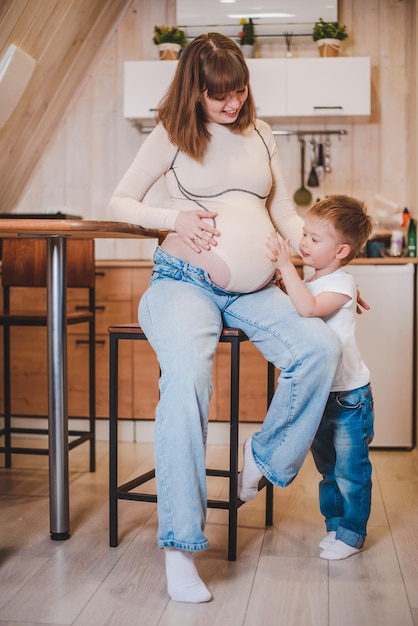 Happy child hugging belly of pregnant woman in kitchen