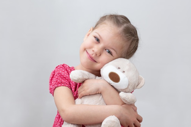 Счастливый ребенок обнимает плюшевого мишку на белом фоне кавказская девочка 5 6 лет в красном