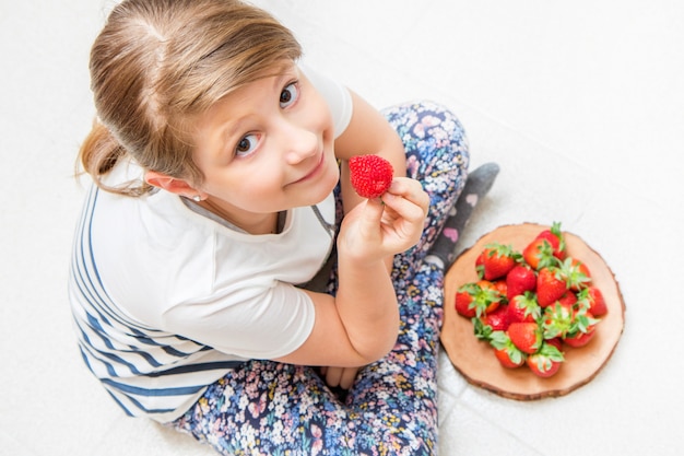 幸せな子供は新鮮なイチゴを食べています