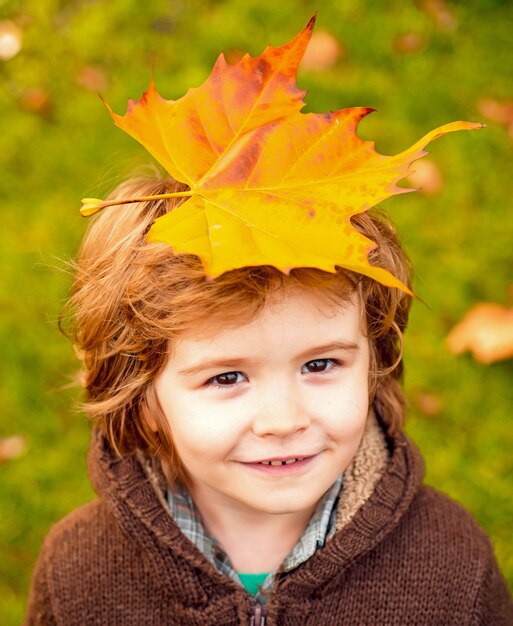 Happy child laughing and playing leaves in autumn outdoors