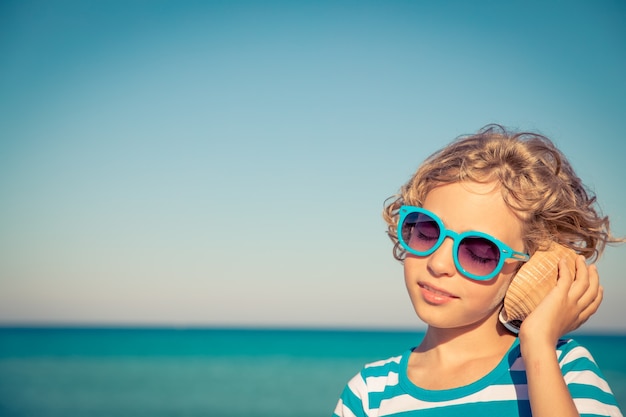 Happy child listen seashell on the beach Kid having fun on summer vacation Healthy active lifestyle concept