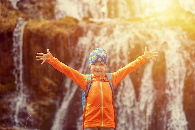 Happy child little girl travel with backpacks near a waterfall Hands to the side Outdoor sports portrait closeup