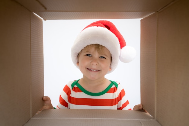 Happy child looking into the box. Funny surprised baby boy unpack Christmas gift box. Xmas holiday concept. Low angle view.