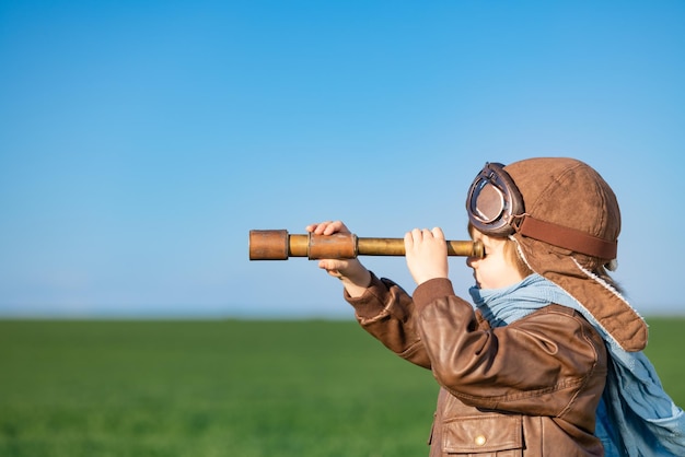 Happy child looking through spyglass outdoor in spring green field Kid having fun against blue sky background Imagination and freedom concept